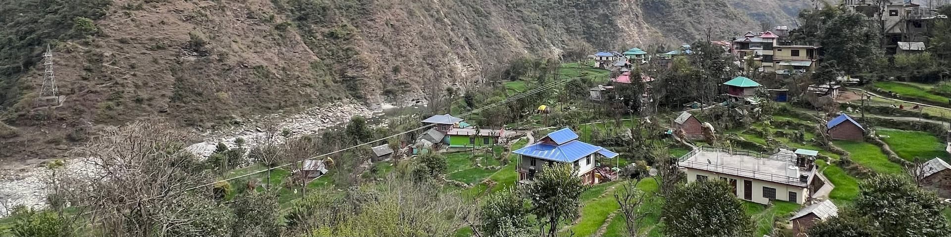 Small village and farmland in Mandi, Himachal Pradesh with cloudy sky and rugged mountains in the back.