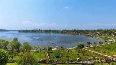 A large lake with boats, a park with trees and a gazebo, and a distant shoreline with buildings.