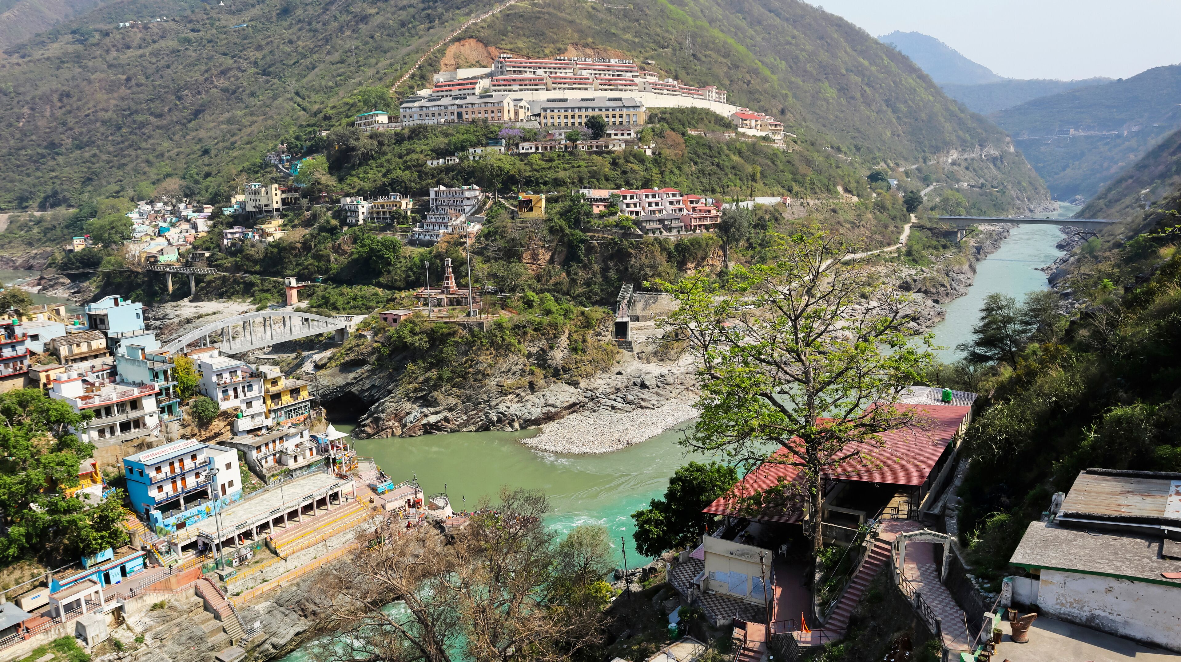 A river flowing through a mountainous area with a bridge, buildings, and a large university on a hill.