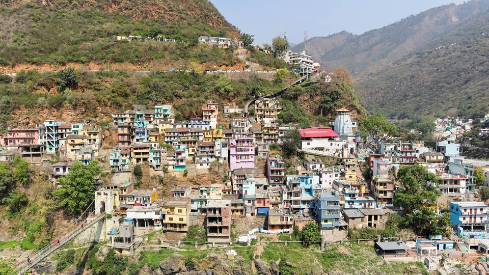 A densely packed hillside settlement with colorful buildings, a prominent school, and a narrow road winding through the terrain.