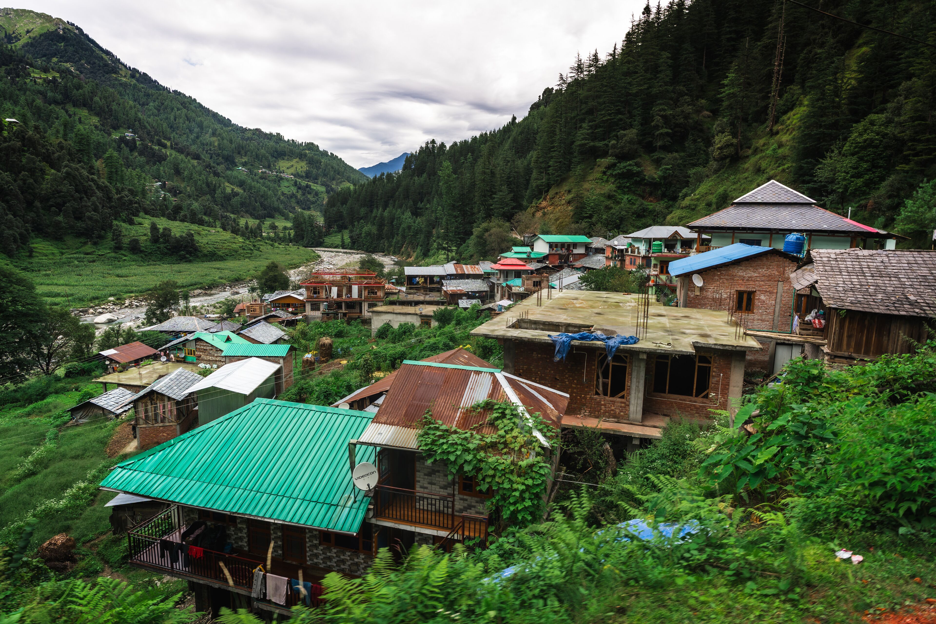 Scenic village view in Barot Valley, Himachal Pradesh, India surrounded by lush green mountains and river.