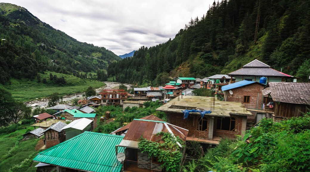 Scenic village view in Barot Valley, Himachal Pradesh, India surrounded by lush green mountains and river.