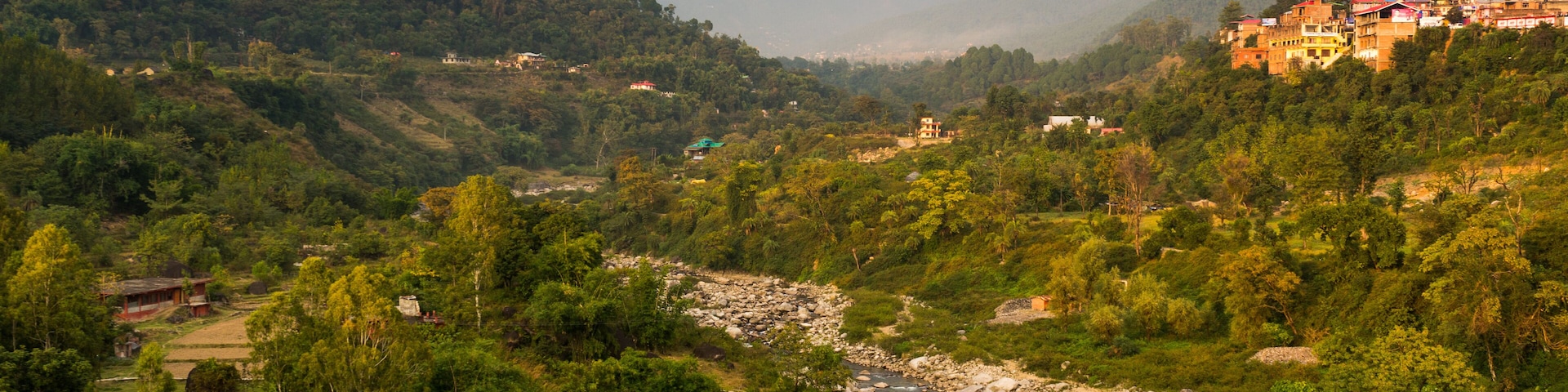 A river winding through a mountainous valley with lush greenery and scattered buildings on the hillsides.