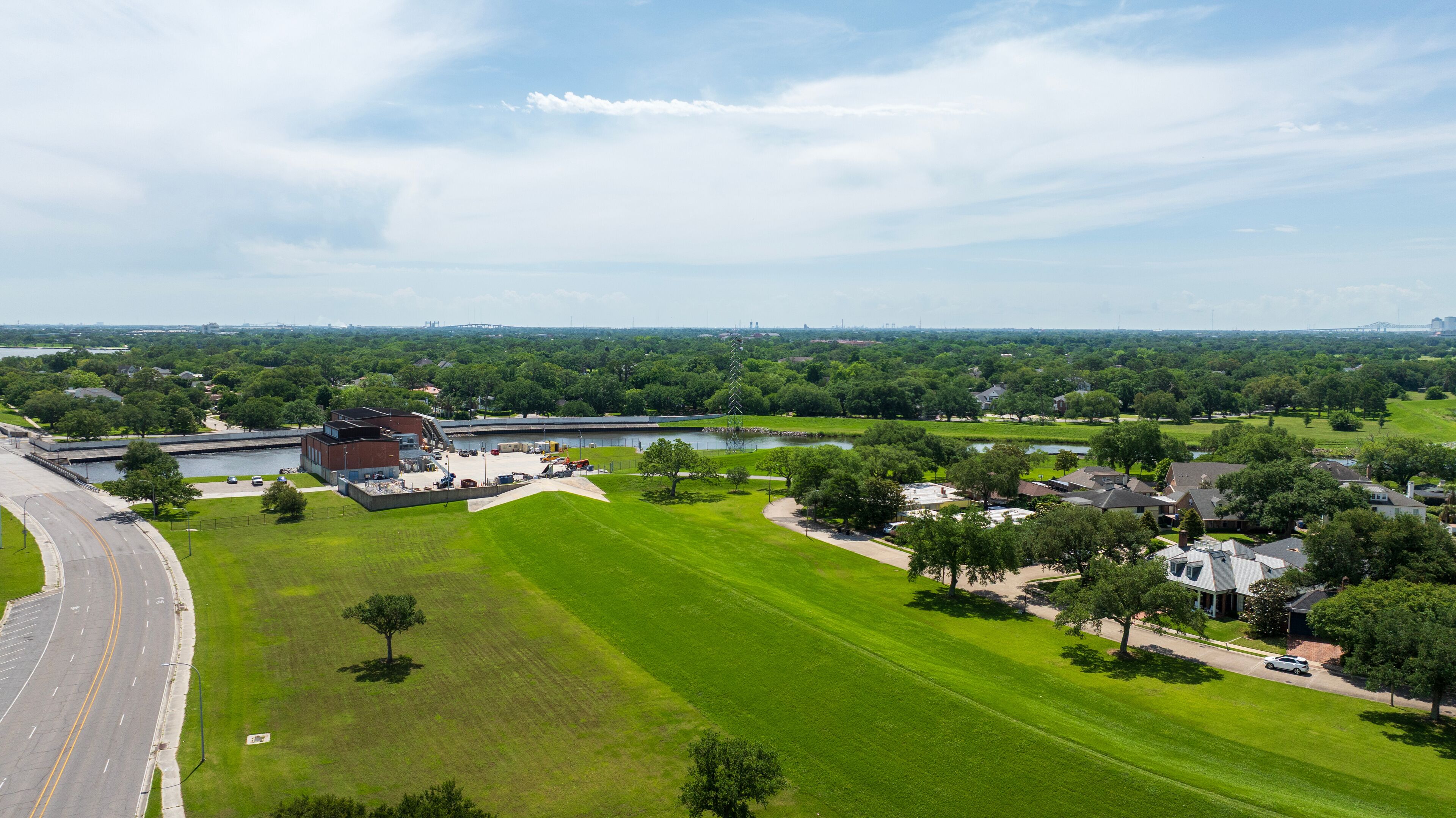 A large green field, a building, a road, and a bridge in the distance.