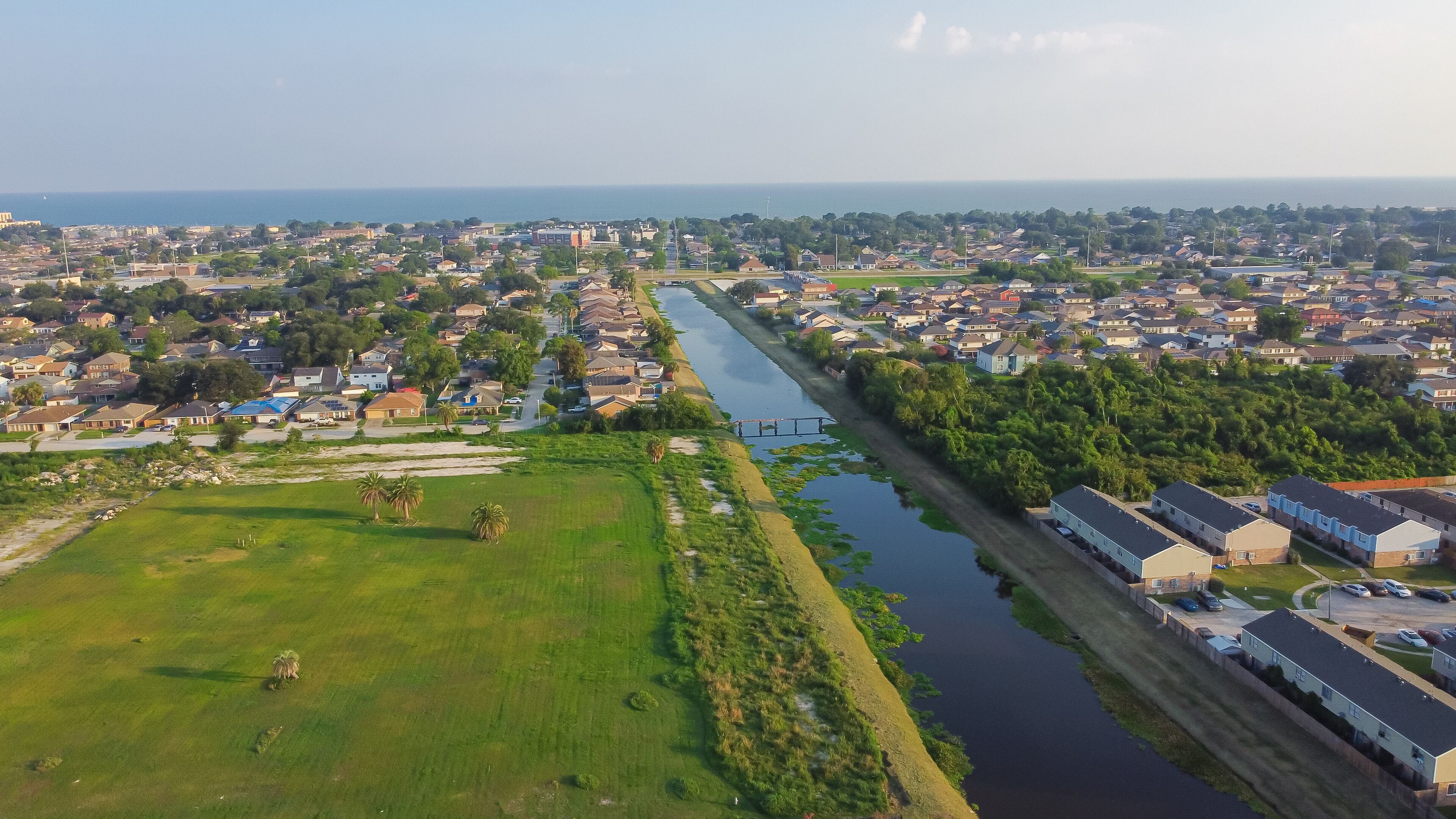 Large vacant land near Farrar Canal with residential houses, duplex townhomes, lush green trees in Little Woods neighborhood toward Lake Pontchartrain in East New Orleans, Louisiana, USA