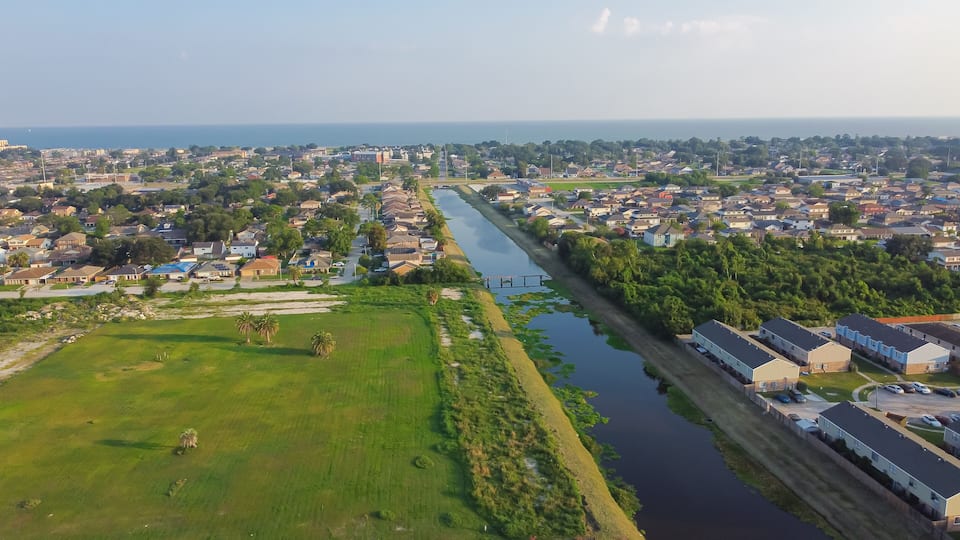 An aerial view of a coastal town with a river running through it, surrounded by residential areas and greenery.