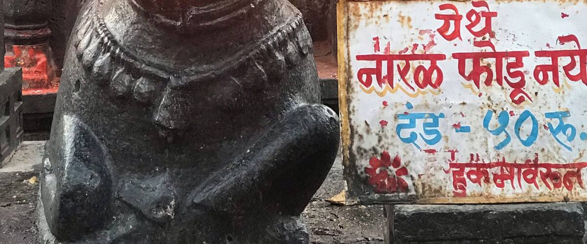 A stone sculpture of a bull with a flame above its head, a sign with text, and a stone structure in the background.