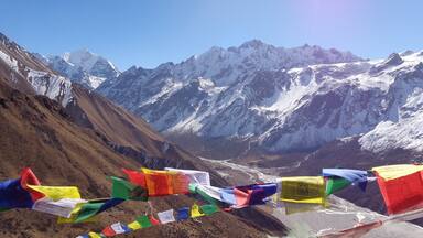 A mountain landscape with snow-capped peaks and colorful prayer flags.