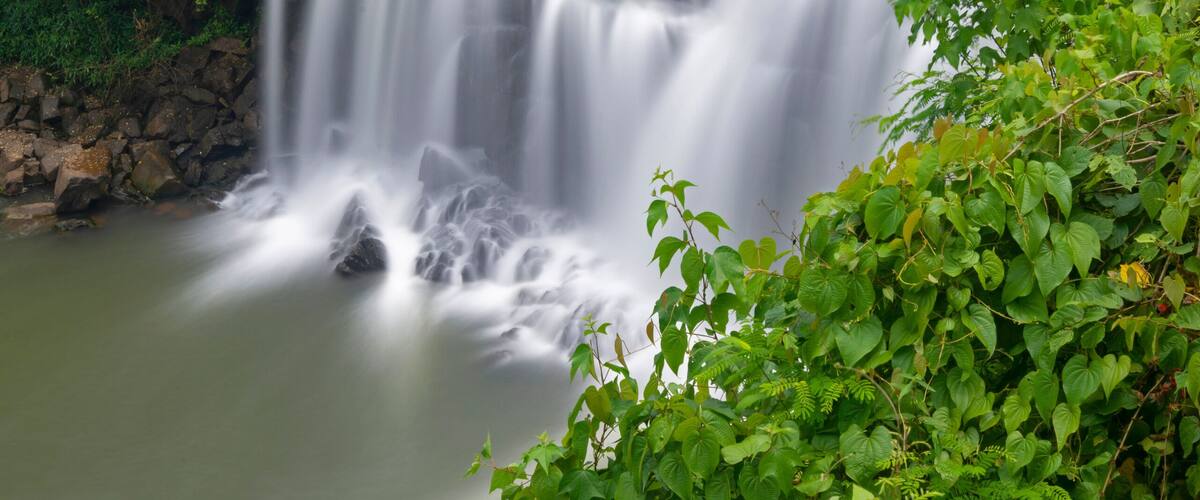 A waterfall cascading over rocks into a river, surrounded by lush greenery.
