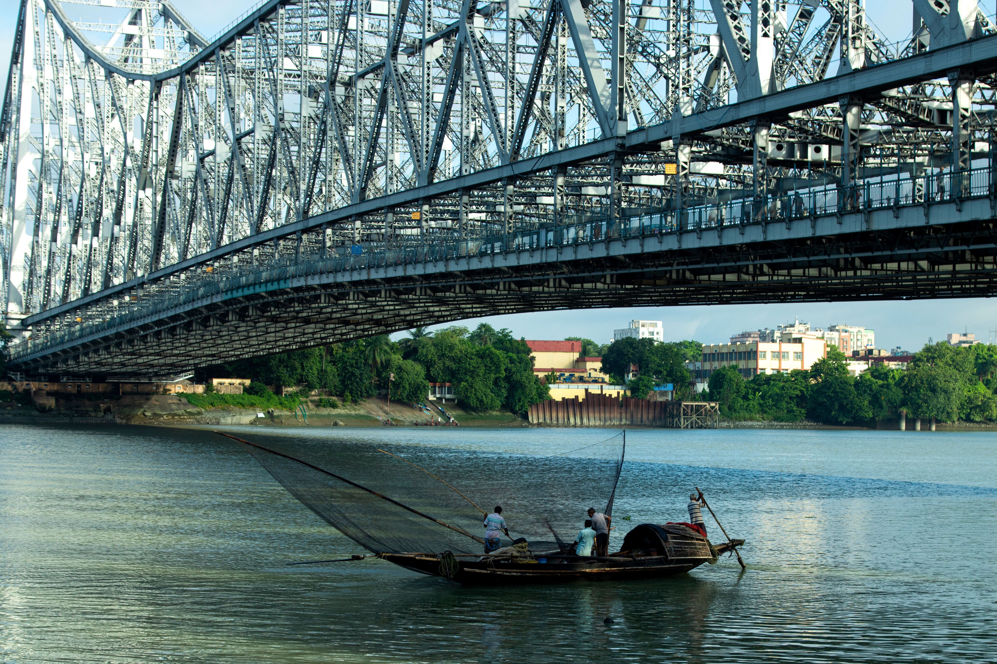 A river with a bridge overhead and a boat with people fishing.