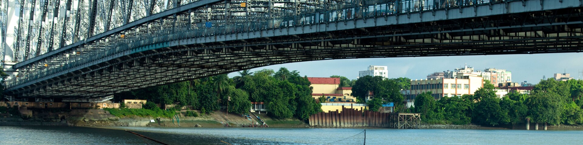 A river with a bridge overhead and a boat with people fishing.
