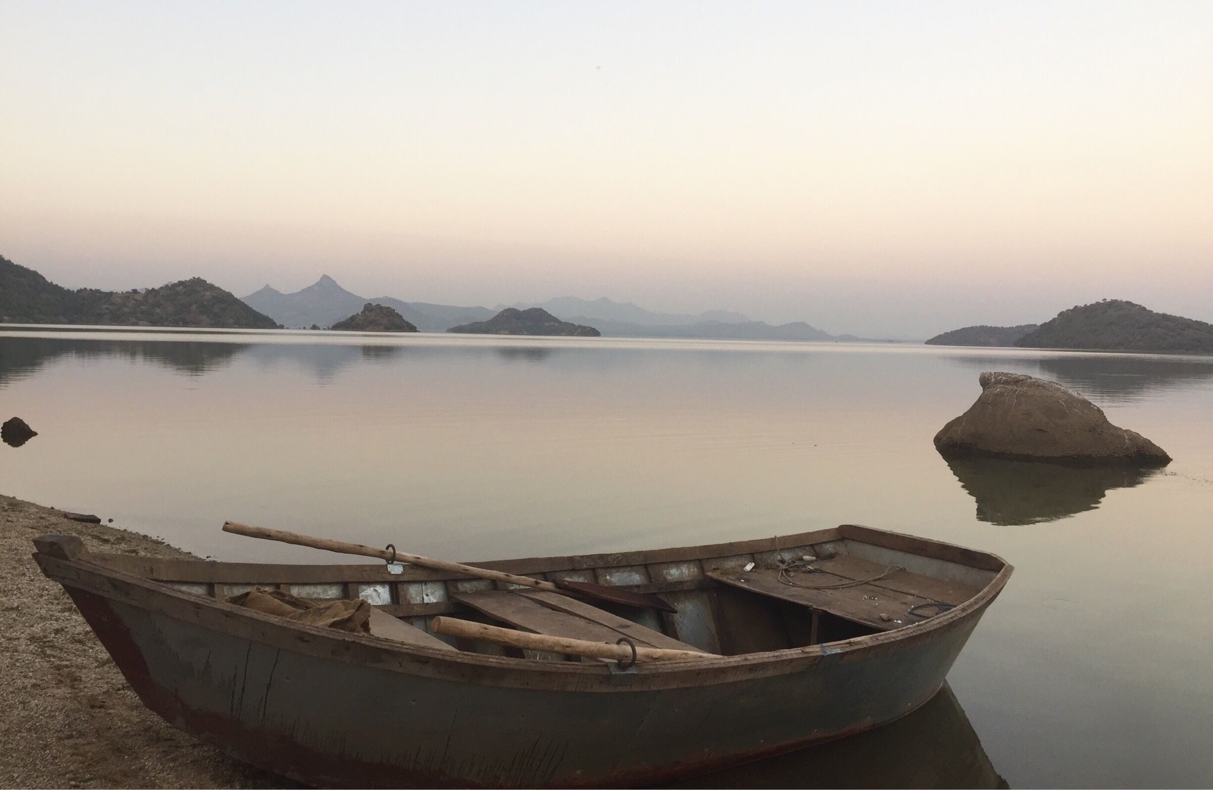 A calm lake with a small boat on the shore and distant mountains.