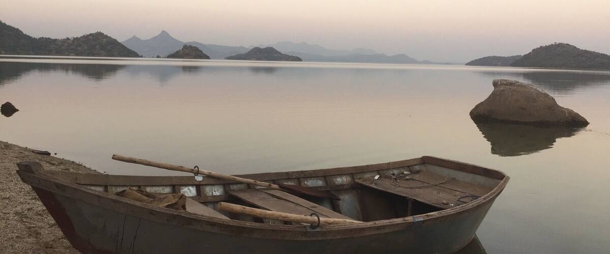 A calm lake with a small boat on the shore and distant mountains.