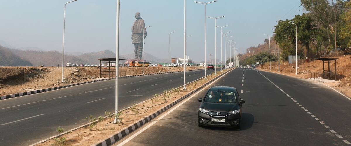 A highway with a large statue on the left, streetlights, and a car driving on the road.
