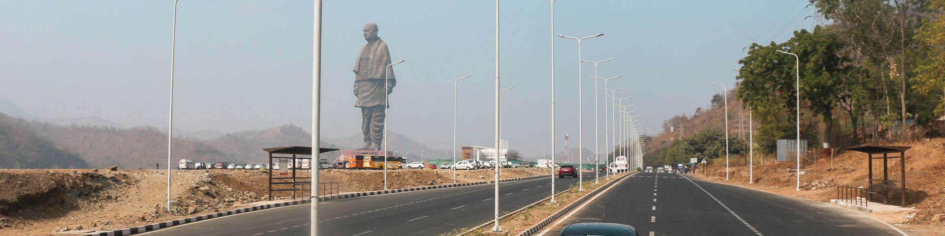 A highway with a large statue on the left, streetlights, and a car driving on the road.