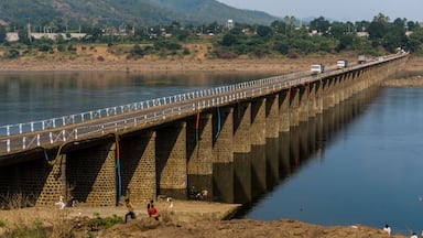 A long bridge over a river with a rocky riverbank and a hilly landscape in the background.