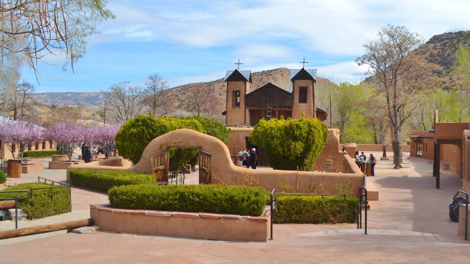 A historic church with a bell tower, surrounded by well-maintained gardens and a mountainous backdrop.
