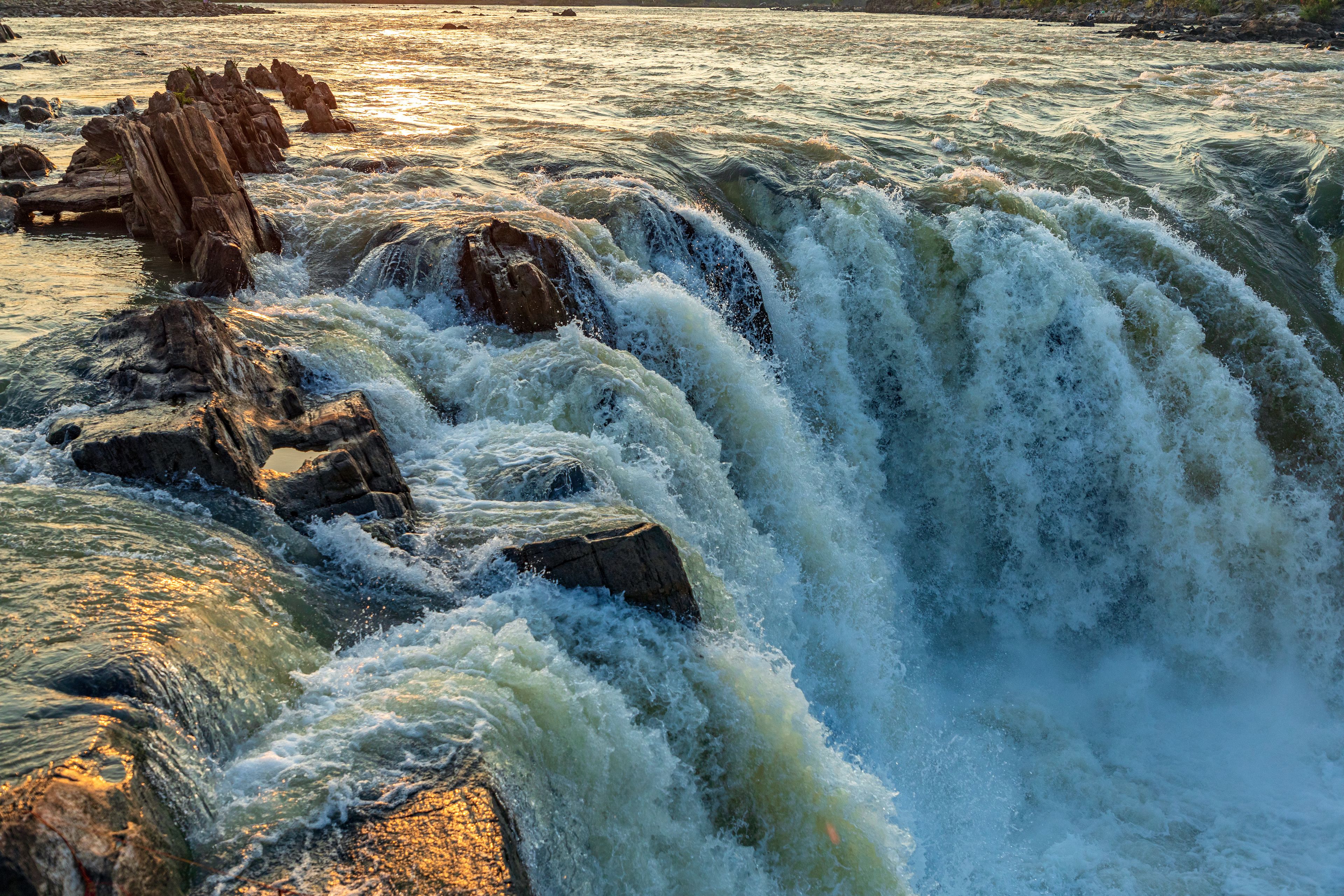 A powerful waterfall cascading over rocks with sunlight reflecting off the water.