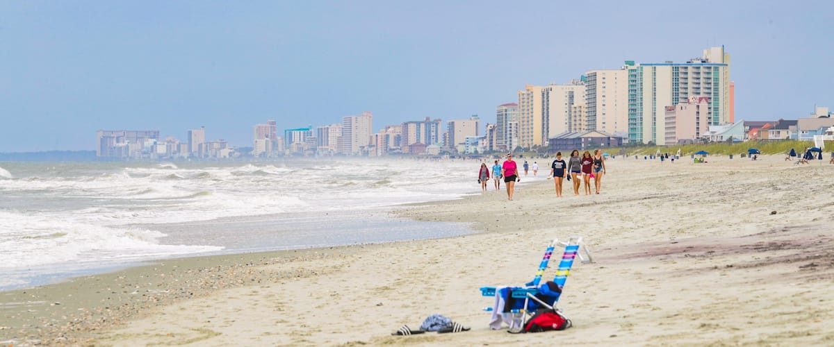 A beach with waves, a row of beach chairs, and a city skyline in the background.
