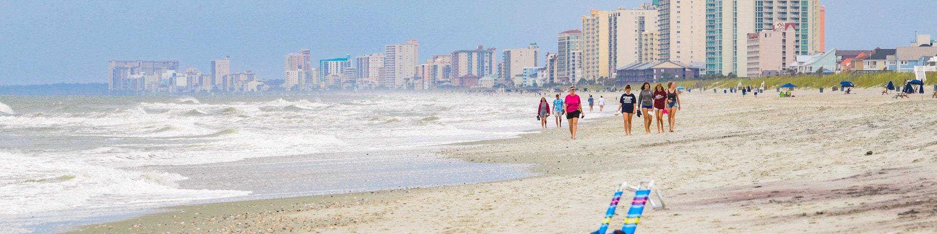 A beach with waves, a row of beach chairs, and a city skyline in the background.