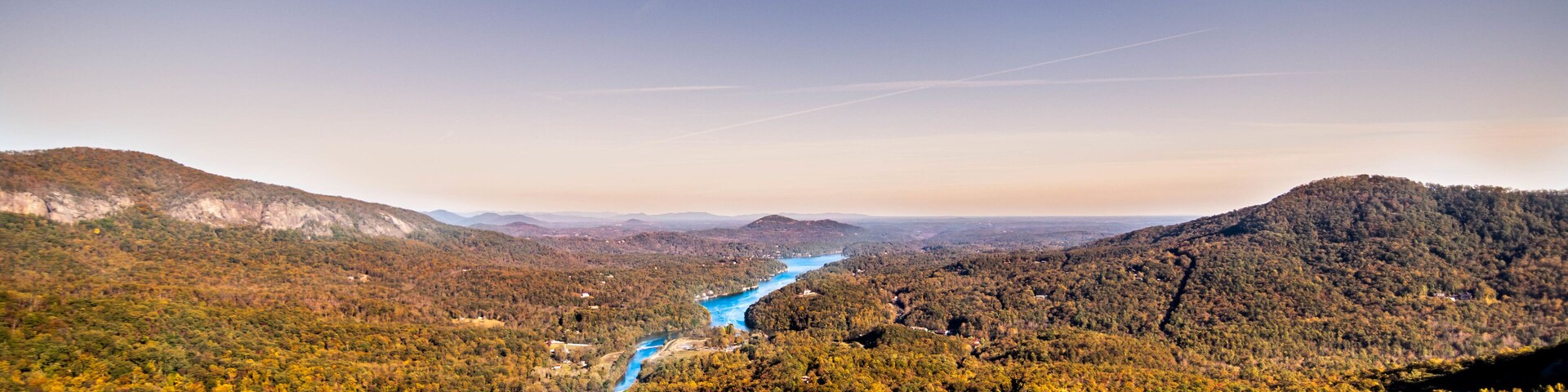 A river winding through a forested valley with autumn foliage and distant mountains.