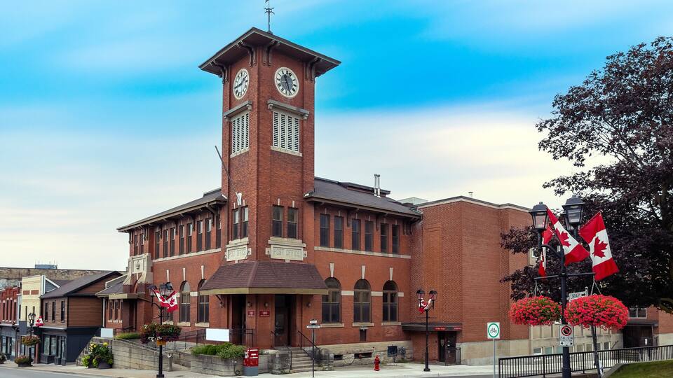 A red brick building with a clock tower, a sign reading "Post Office," and Canadian flags.