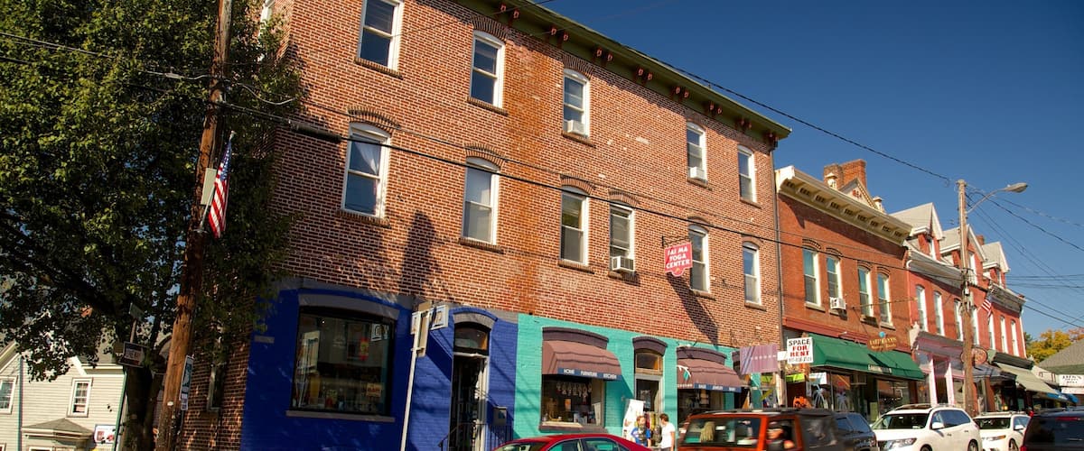 A street with brick buildings, a red car, and a white SUV.