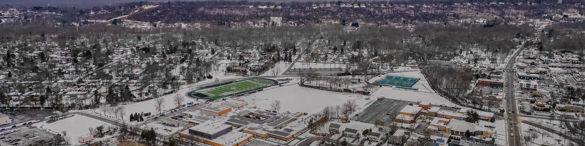 Aerial drone view of New Providence, New Jersey, covered in snow. The frozen landscape highlights roads, homes, and infrastructure, showcasing the suburban town in the cold season.