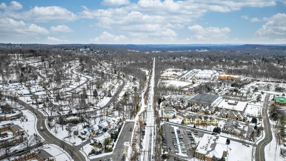Aerial drone view of New Providence, New Jersey, covered in snow. The frozen landscape highlights roads, homes, and infrastructure, showcasing the suburban town in the cold season.