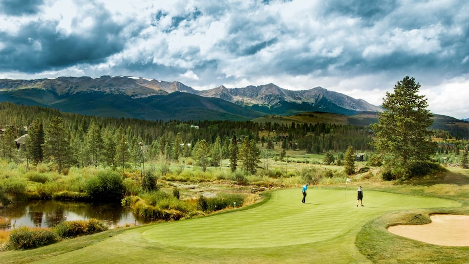 A golf course with a lake, forest, and mountains in the background.