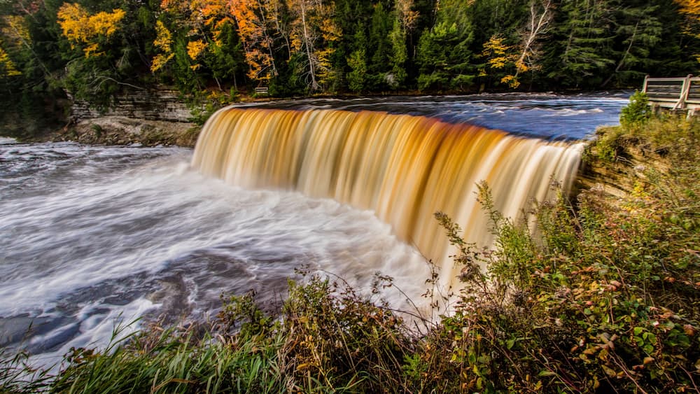 A waterfall cascading over a rocky cliff surrounded by autumn foliage.