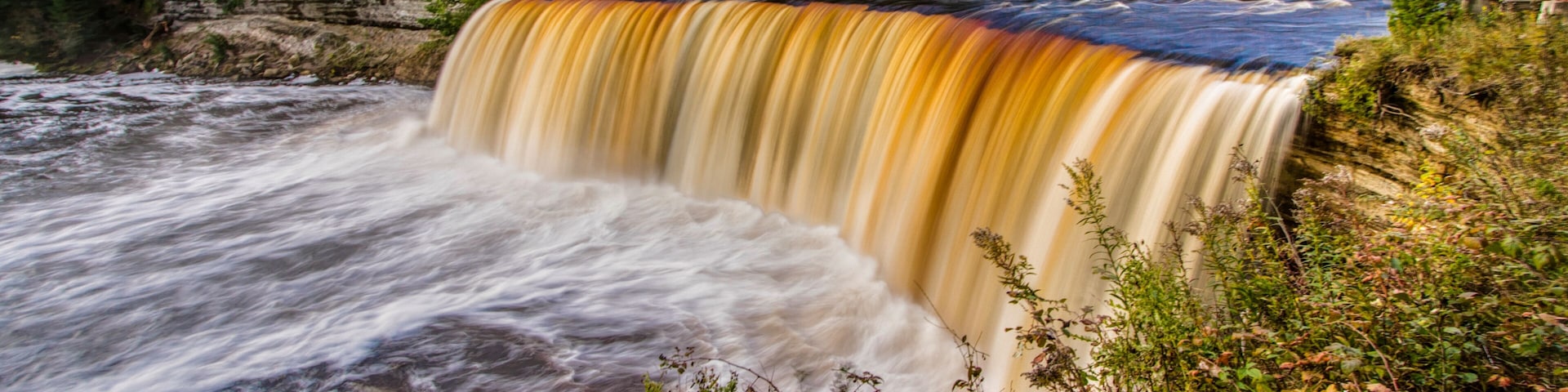 A waterfall cascading over a rocky cliff surrounded by autumn foliage.