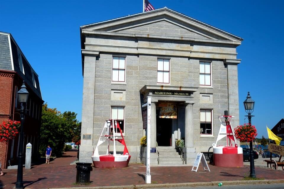 Edifício de um museu marítimo com estilo arquitetônico clássico, exibindo uma bandeira americana em destaque e uma placa.