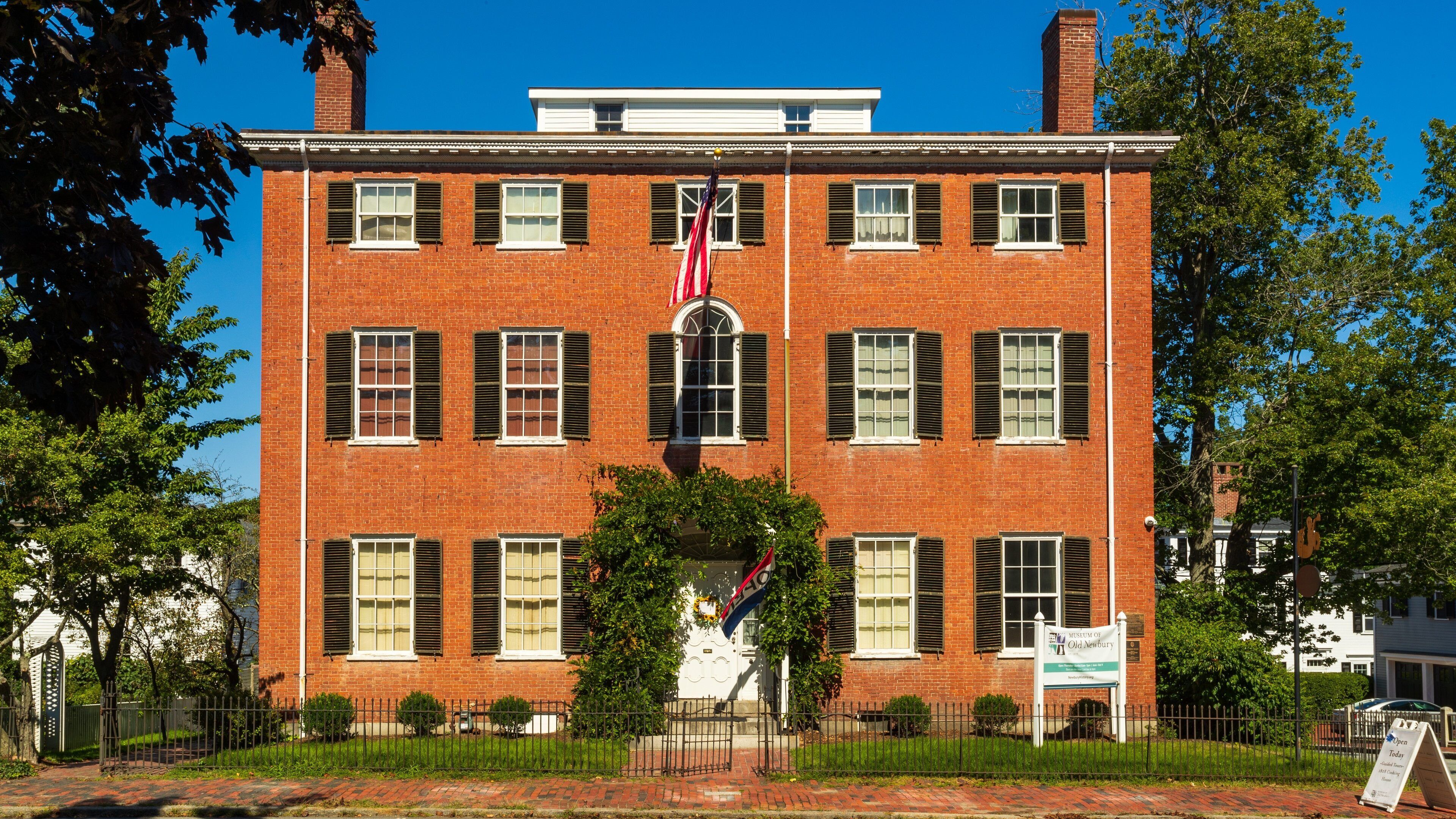 A red brick building with white shutters, a flag, and a sign for the Museum of Old Newbury.