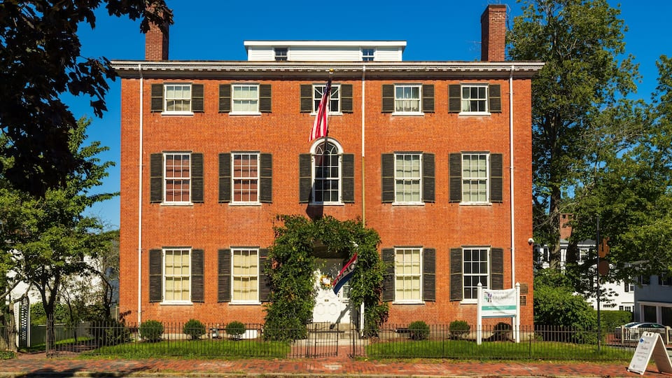 A red brick building with white shutters, a flag, and a sign for the Museum of Old Newbury.