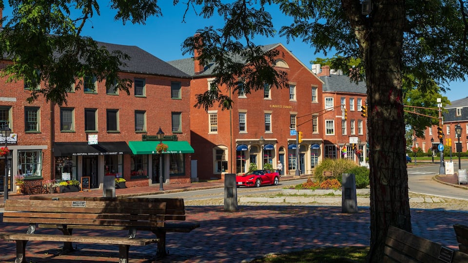 A brick building with a green awning, a red car parked in front, and a bench on the sidewalk.