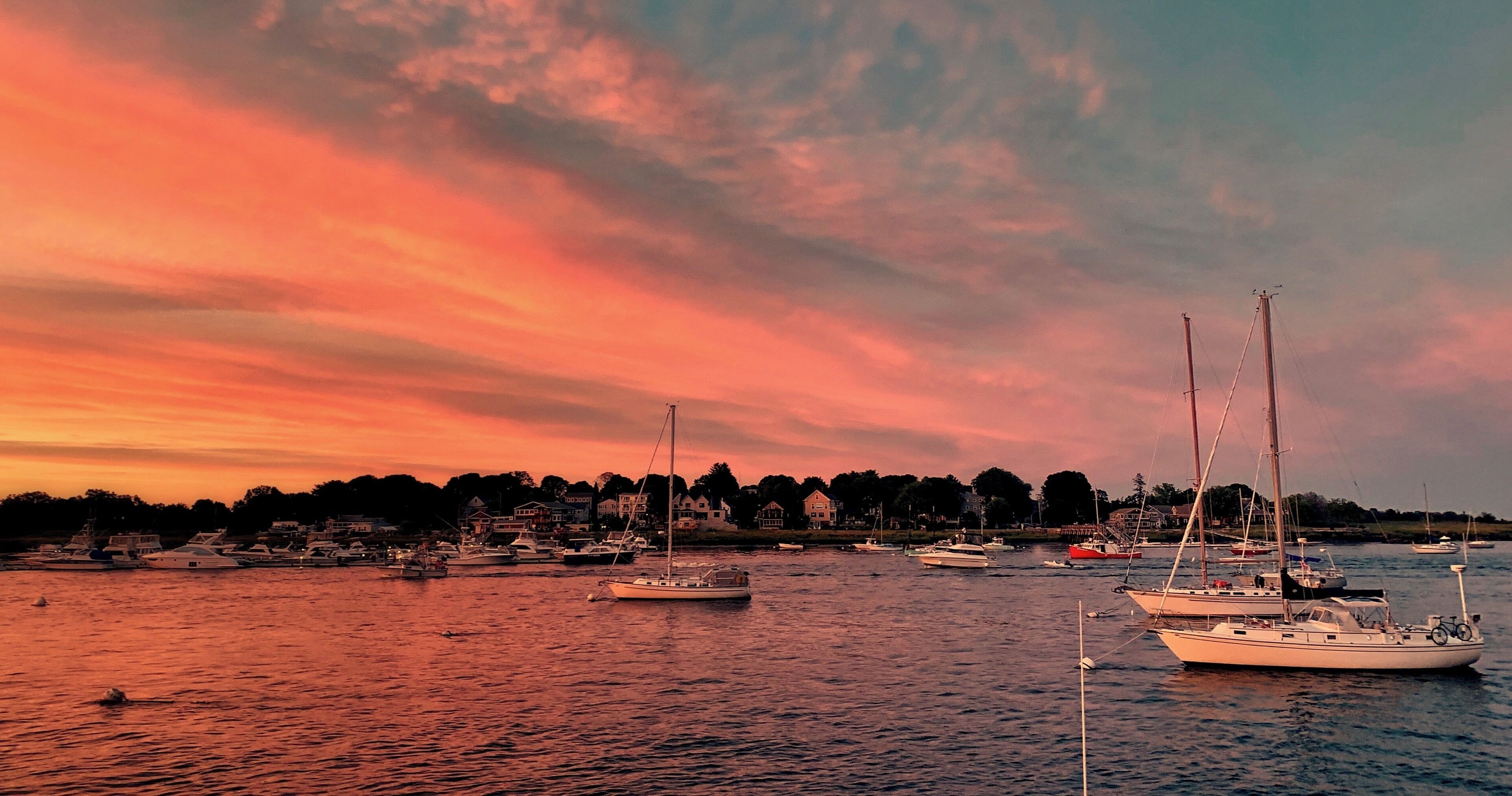 A marina with several sailboats and yachts during sunset.