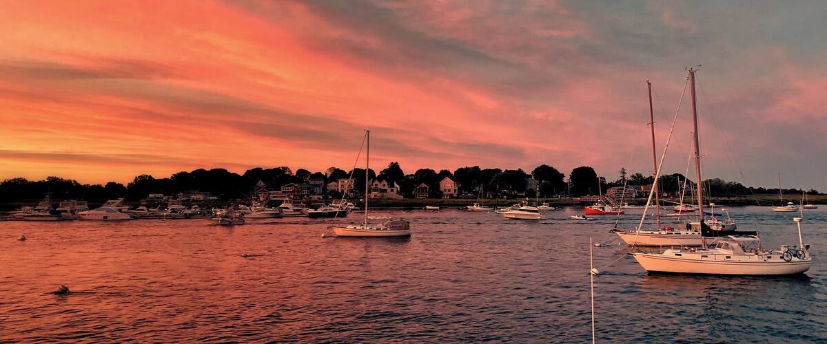 A marina with several sailboats and yachts during sunset.