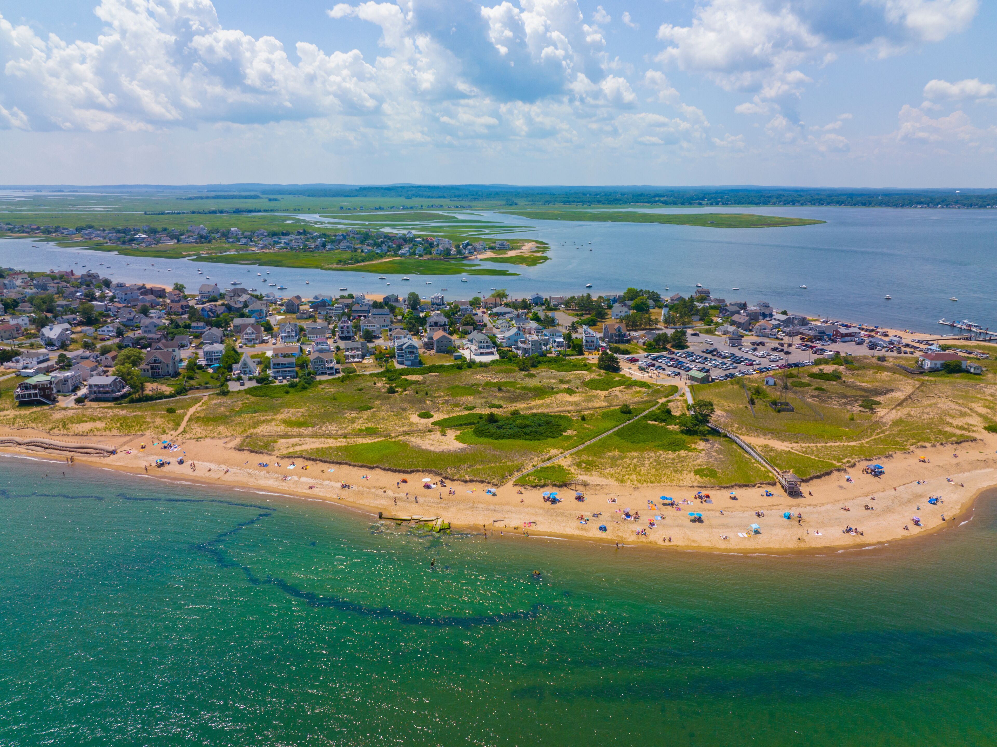 An aerial view of a coastal town with a beach, houses, and a marina.