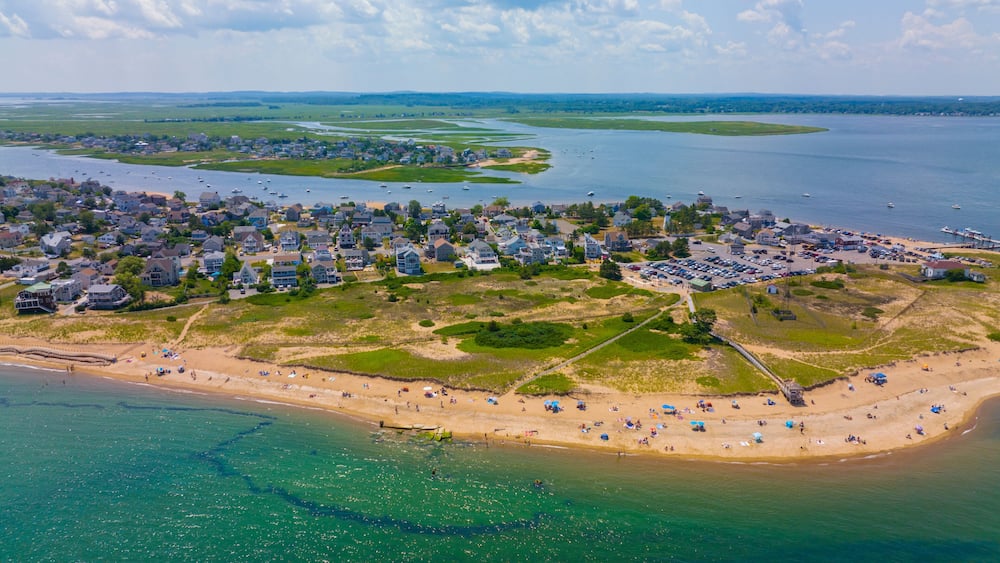 An aerial view of a coastal town with a beach, houses, and a marina.