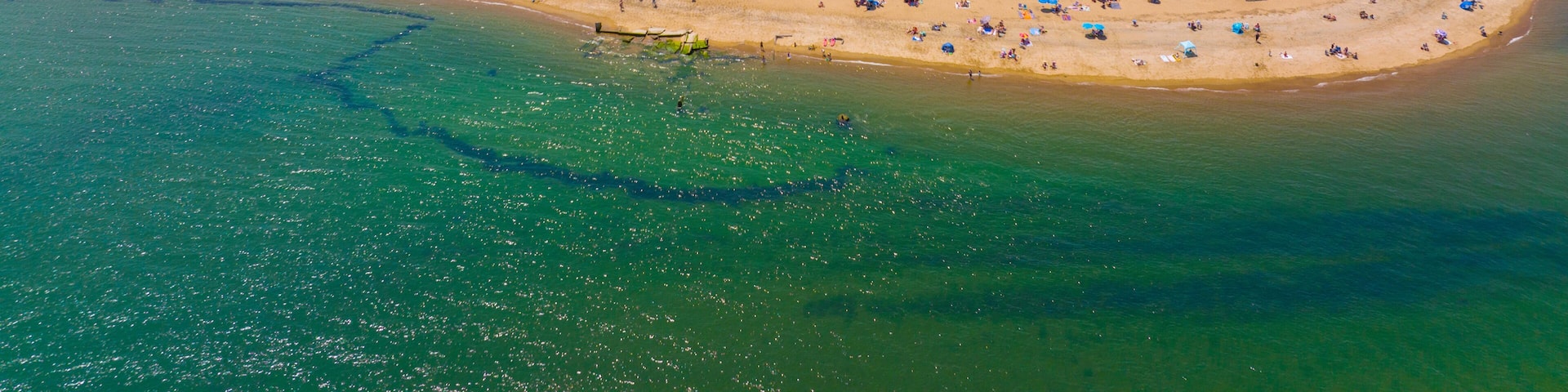 An aerial view of a coastal town with a beach, houses, and a marina.