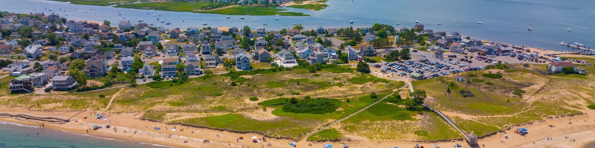 Vista aérea de un pueblo costero con playa, casas y un puerto deportivo.