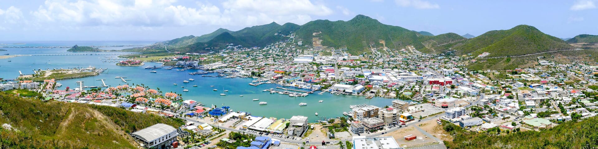 A coastal town with a marina, mountains in the background, and a clear sky.