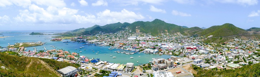 Un pueblo costero con un puerto deportivo, montañas al fondo y un cielo despejado.