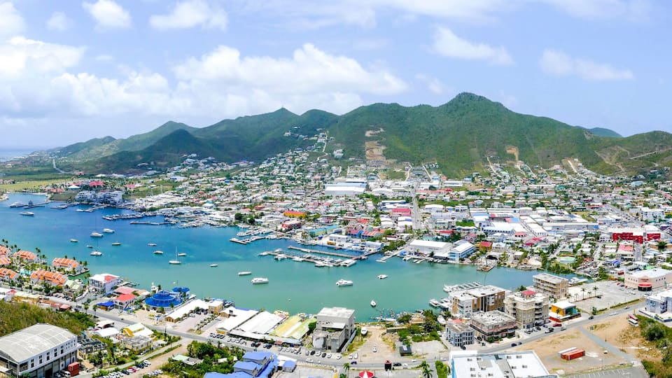 A coastal town with a marina, mountains in the background, and a clear sky.