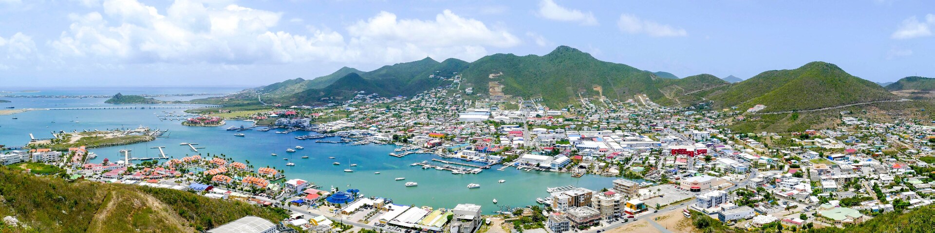 Un pueblo costero con un puerto deportivo, montañas al fondo y un cielo despejado.