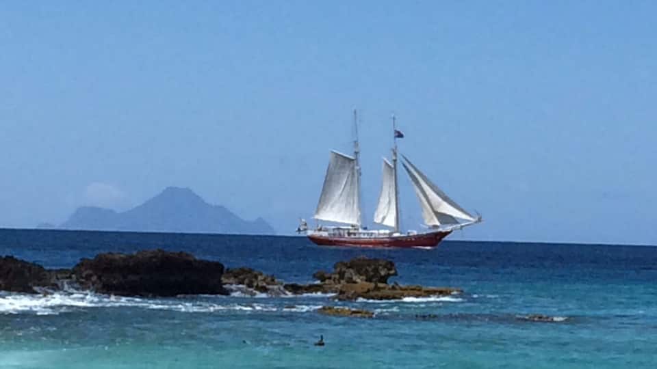 A sailboat near rocky coastline with clear turquoise water.