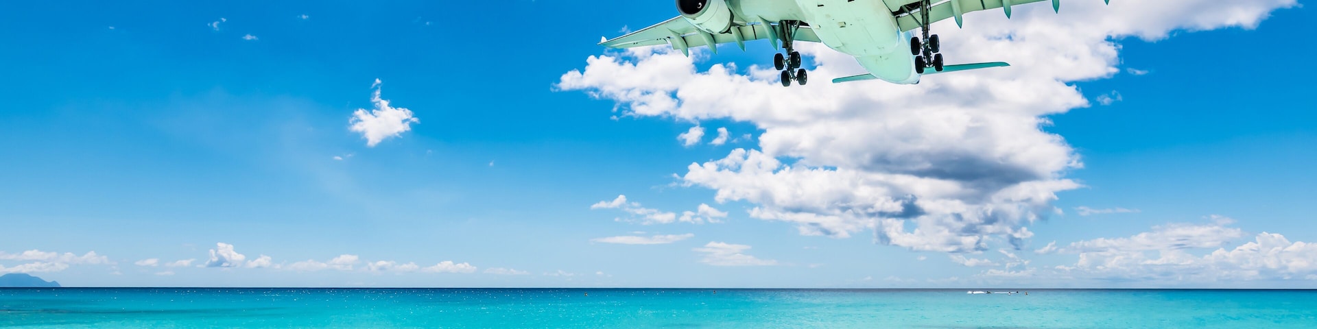 Céu azul límpido, mar turquesa e um avião sobrevoando uma praia.