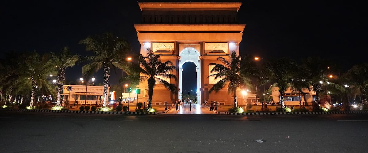 A well-lit archway with palm trees and street lamps.
