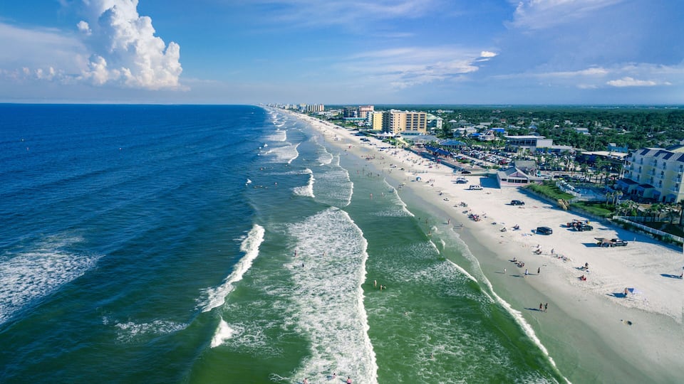 A coastal cityscape with a beach, ocean waves, and buildings along the shore.